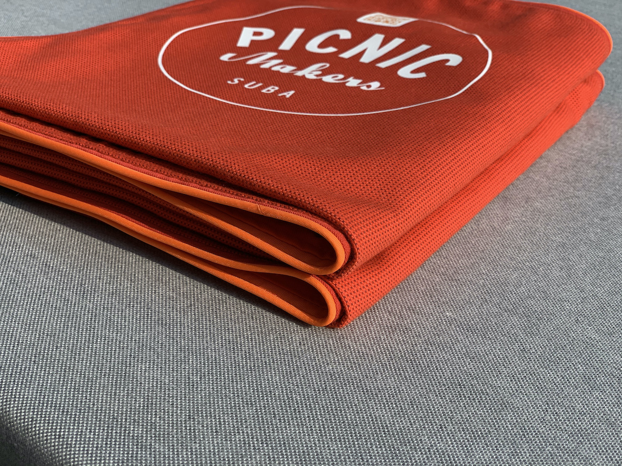 Dynamic, elegant perspective of a perfectly folded suba.blanket.red, showcasing the logo and the clean line of the orange piping