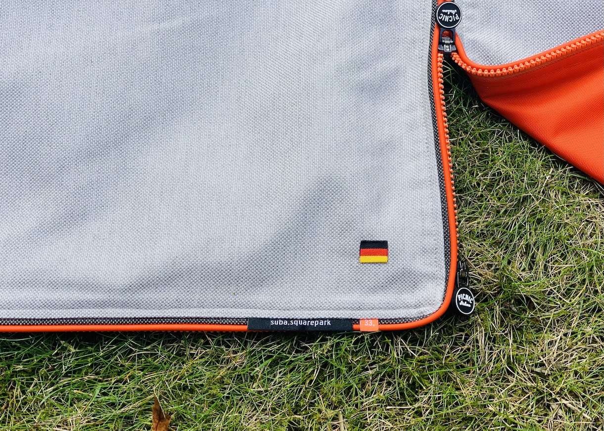 Close-up of the corner of the suba.squarepark.33 blanket featuring the integrated zip system, premium stitching details, and a small German flag label — highlighting precision craftsmanship and Made in Germany quality.